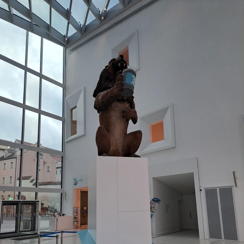 A lion statue holding a blue cup. The sculpture is inside a building with large windows.